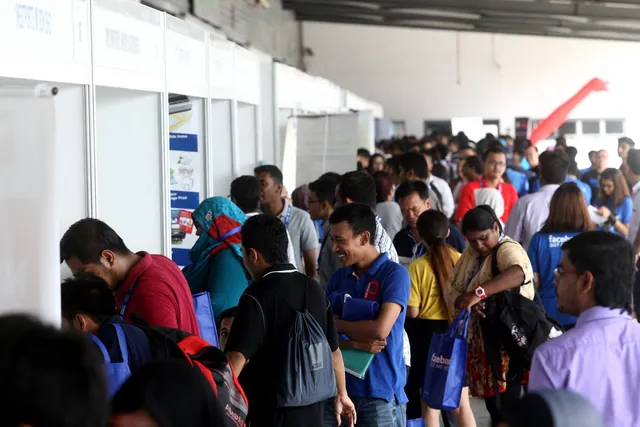 Crowds of job seekers with lanyards and blue Facebook Got Me Hired bags queuing along a row of employer booths